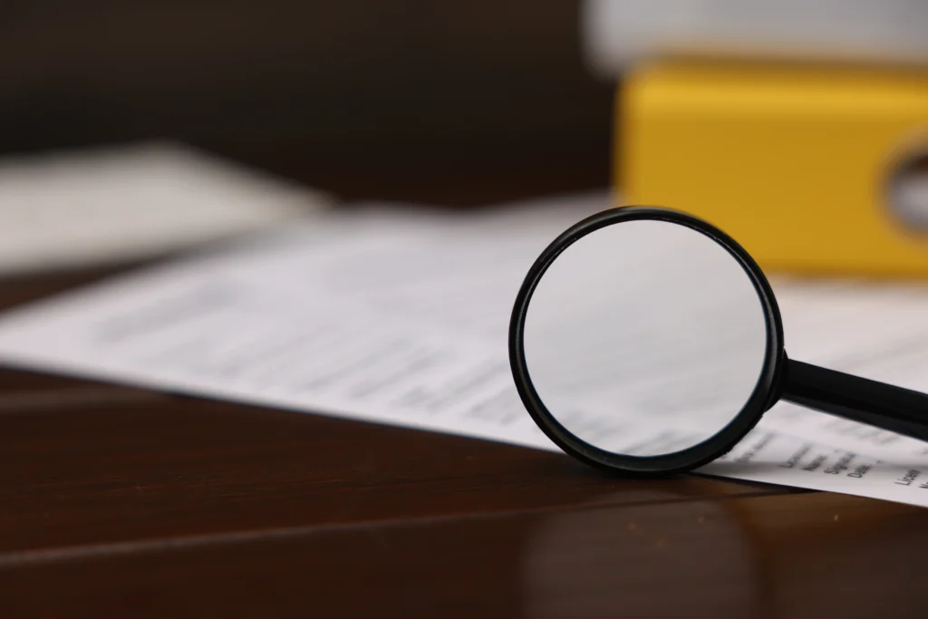 Vista de cerca de una lupa analizando detalladamente formularios y documentos legales de inmigración sobre un escritorio.